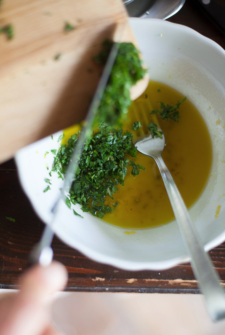 Adding chopped herbs to a bowl of olive oil