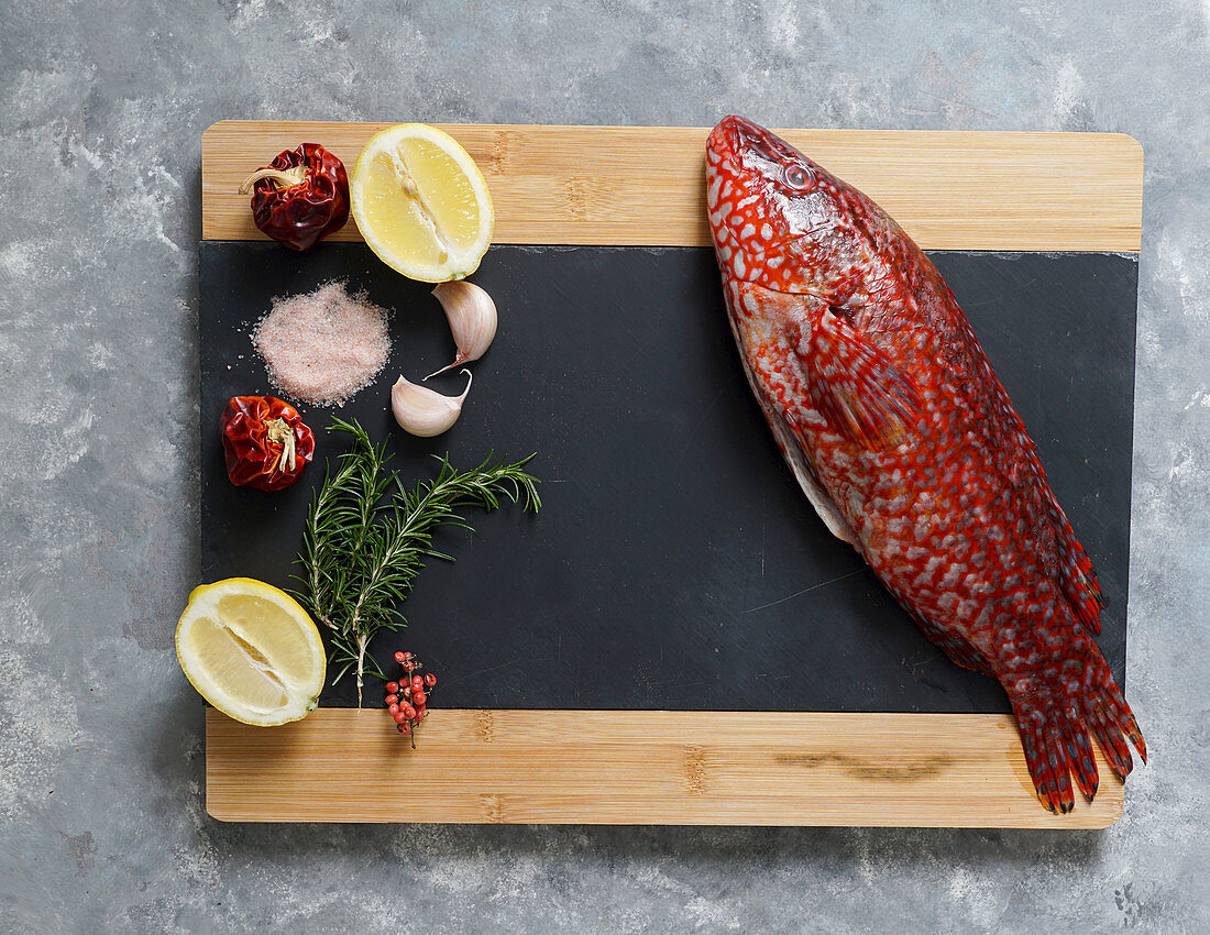 Roter Ballan-Lippfisch mit Zutaten auf Schiefertafel