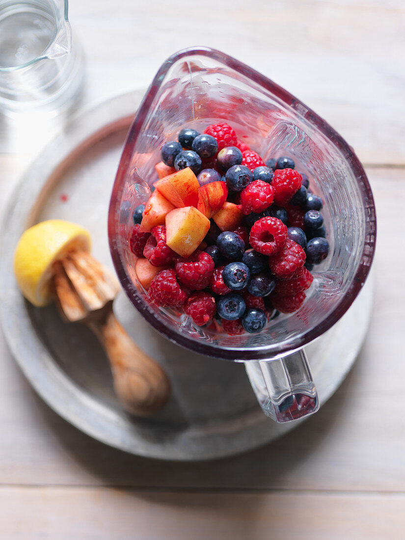 Ingredients for a smoothie (raspberry, blueberry, apple, lemon) in a blender
