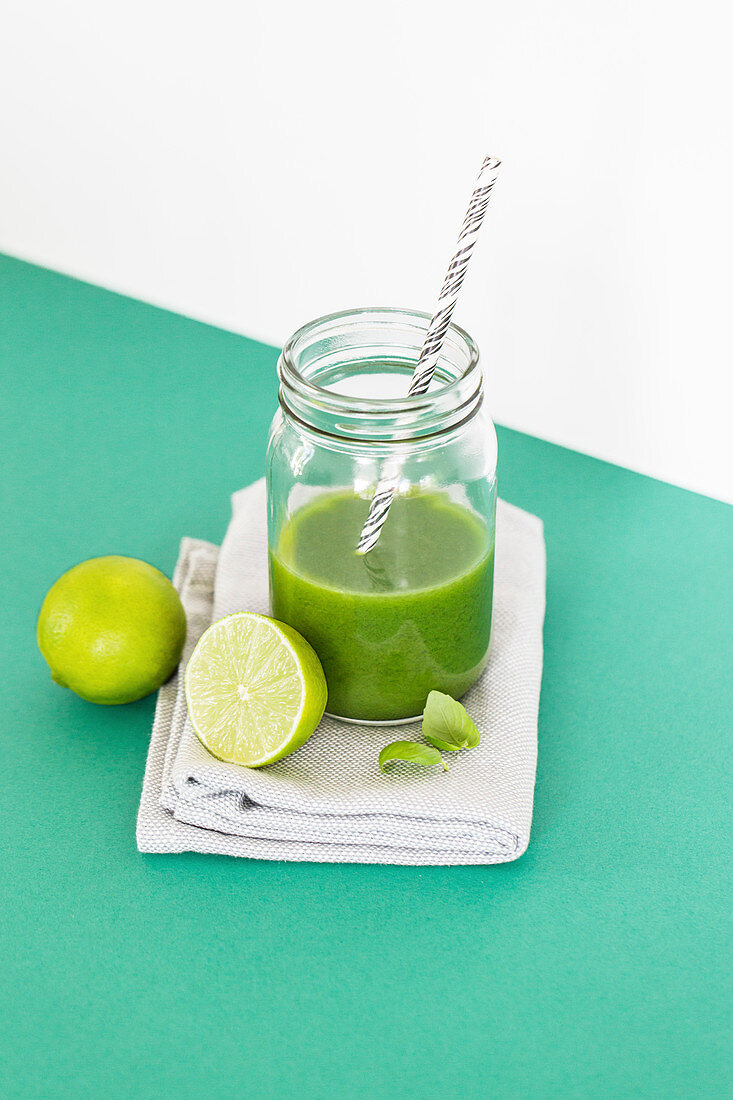 A green lime and basil smoothie in a glass with a straw
