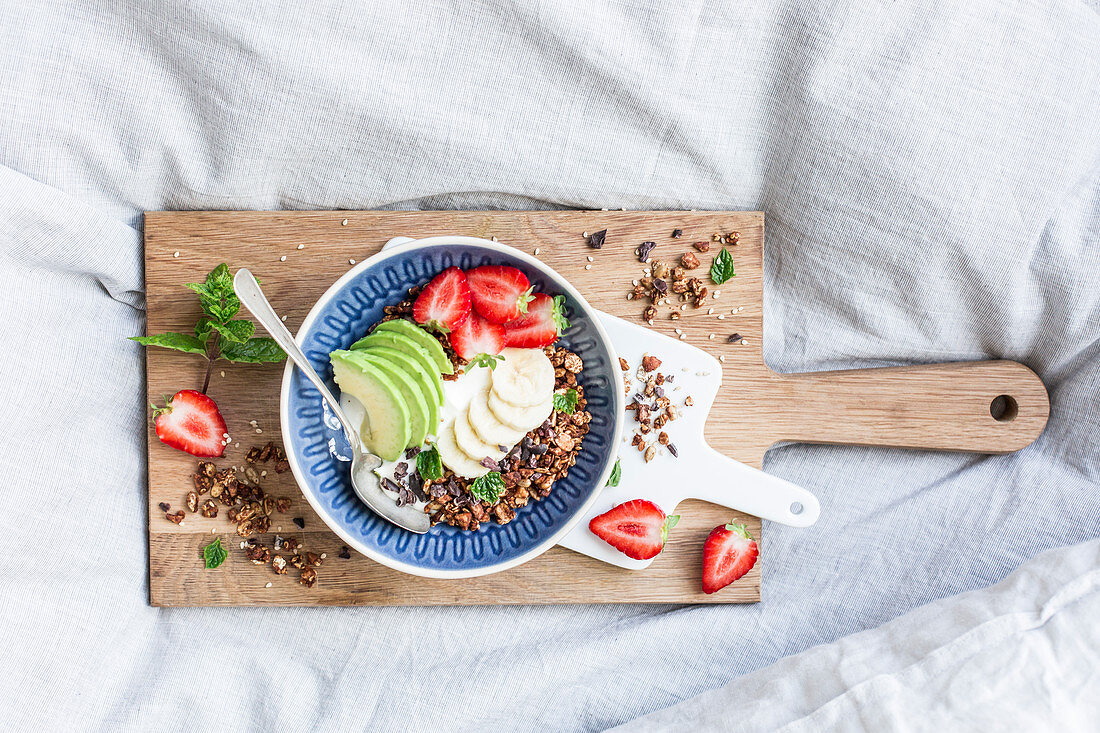 Mandel-Sesam-Granola mit Erdbeeren und Avocado auf Holzbrett im Bett