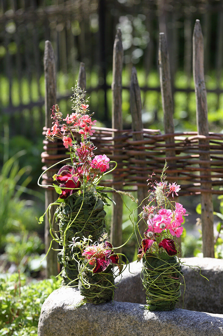 Geraniums and coleus in vases decoratively wrapped in leaves and grasses