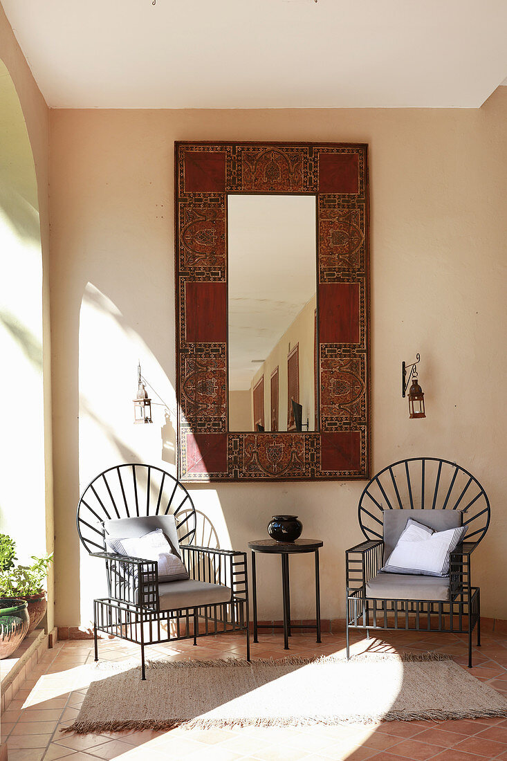 Two modern metal chairs below Oriental mirror on wall