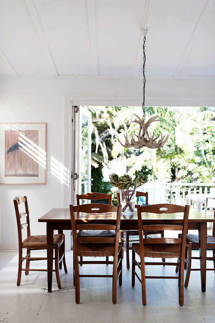 Wooden furniture in white dining room with open terrace windows leading onto balcony