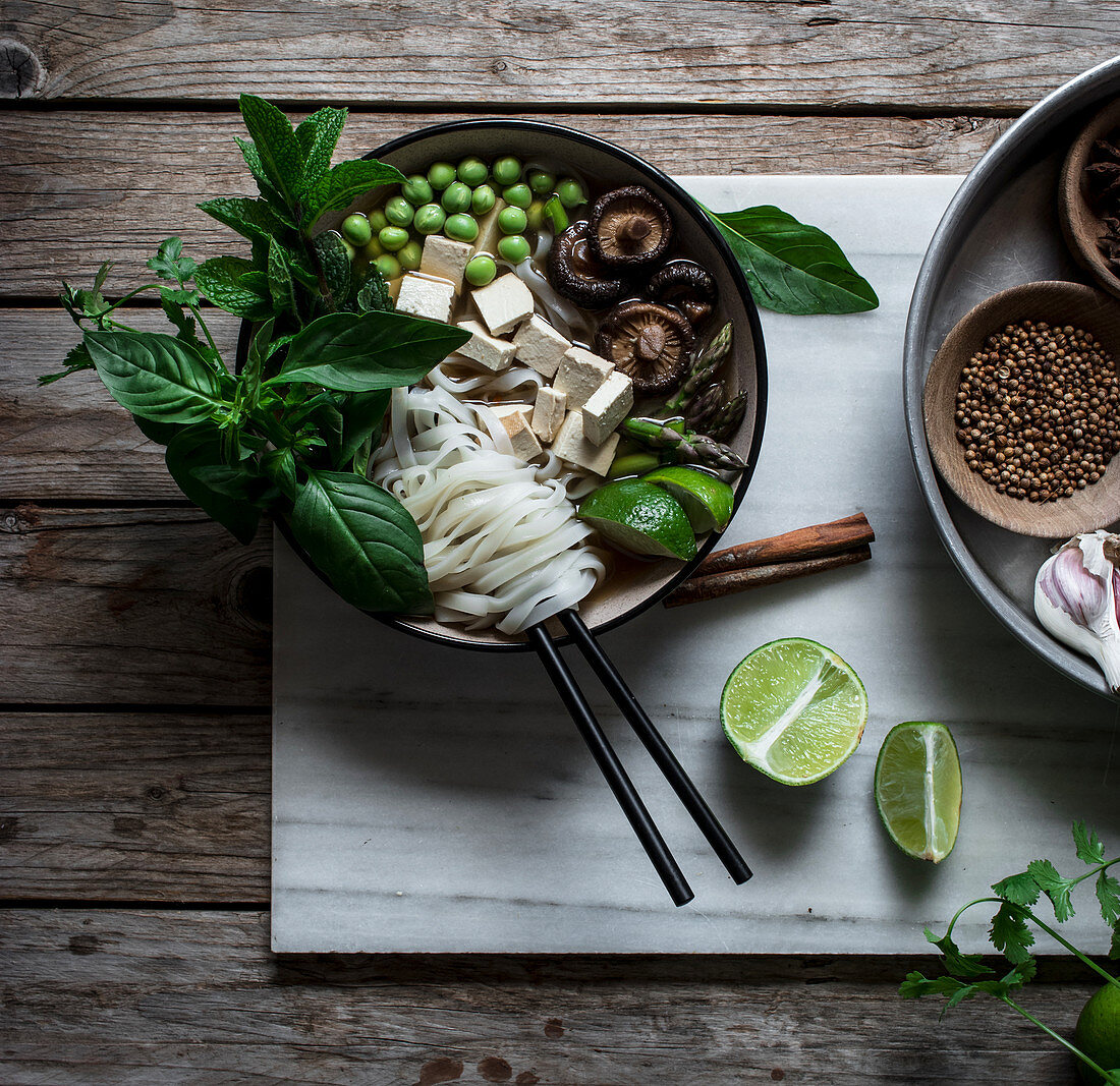 From above of arranged bowls with dry spices and served Pho soup with noodles on marble board