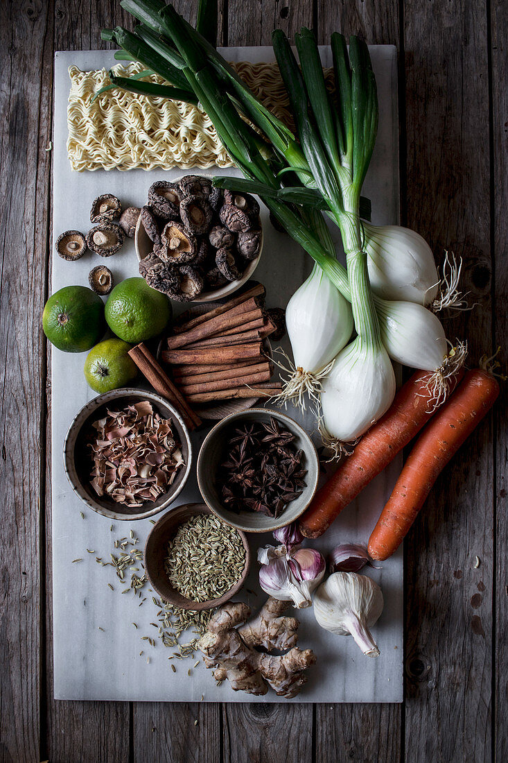From above of board with fresh vegetables and spices with dry noodles for cooking traditional Pho soup