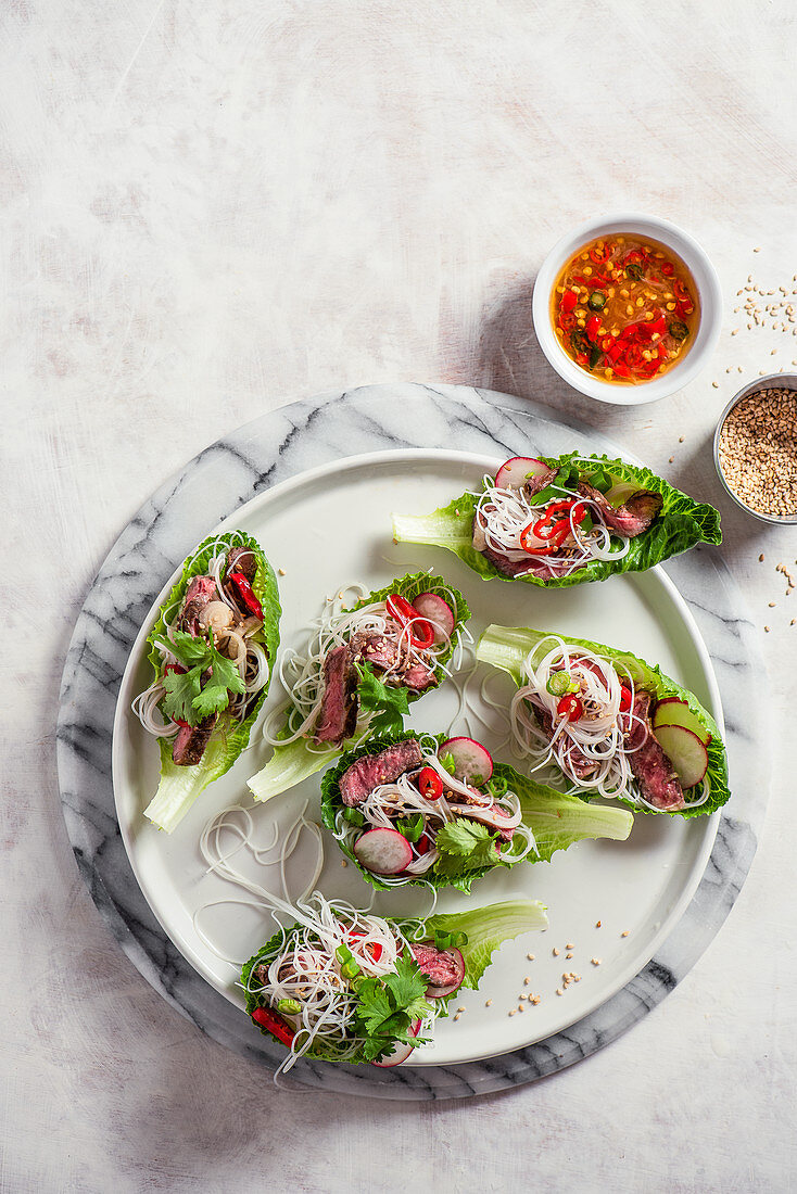 Lettuce cups with oriental beef and noodle salad with spring onion, chilli, radish, coriander. Chili and lime sauce on a side