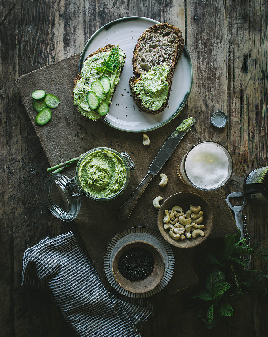 From above toasts with green cashew pate and slices of cucumber on wooden board