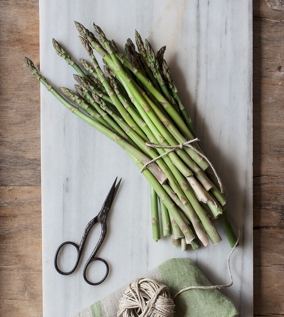 Top view of marble board with pile of asparagus tied with twine rope on wooden table