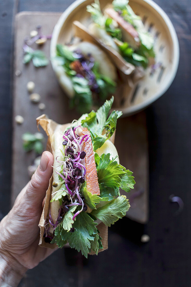 Hände halten Gua Bao Sandwich mit frischer Petersilie