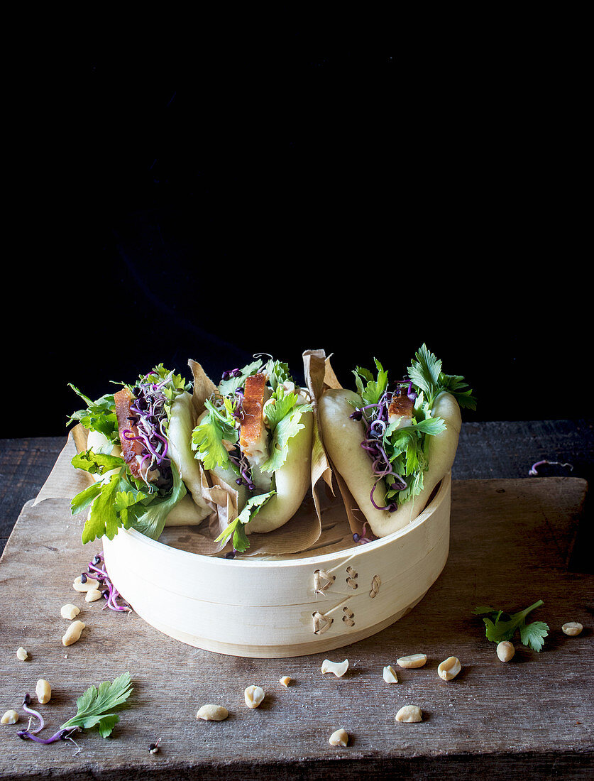 Row of Gua Bao sandwiches in lotus leaf bread filled with bacon and parsley served on bamboo steamer