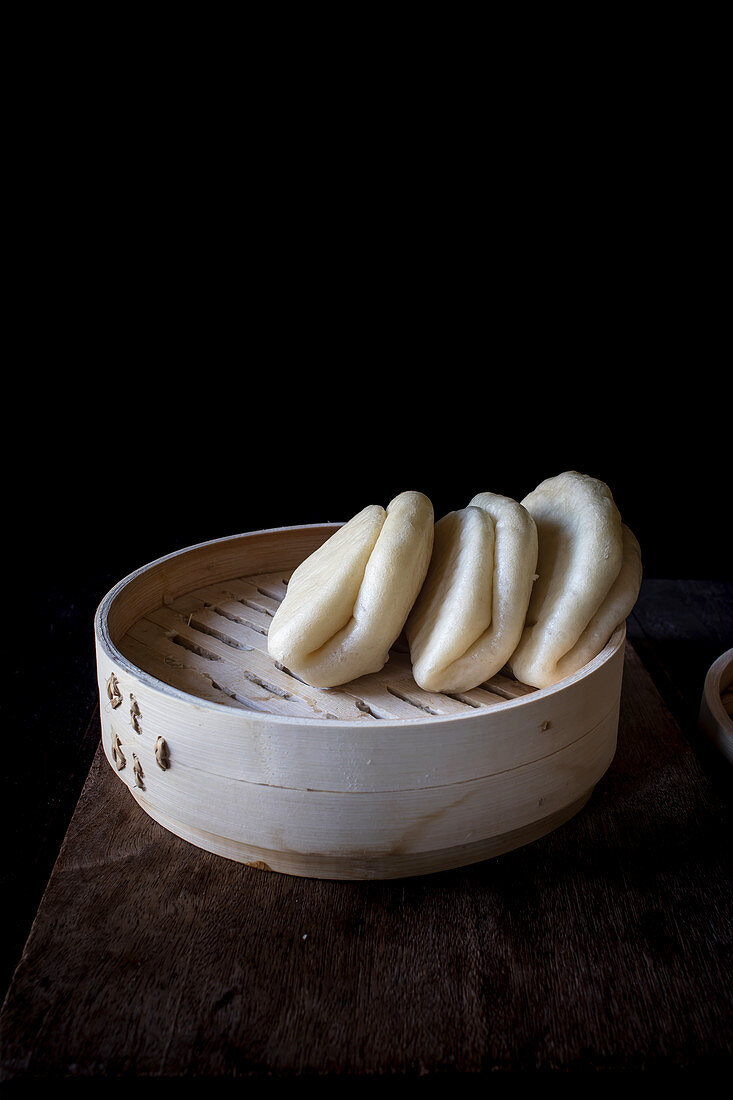 Bamboo steamer with raw lotus leaf buns for Gua Bao at table