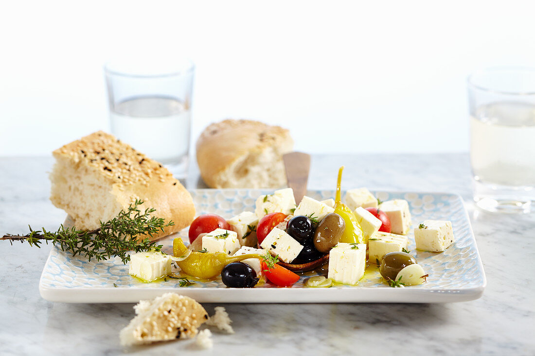 In Olivenöl eingelegter Feta mit Tomaten, Knoblauch, Peperoni und Oliven, dazu Sesam-Fladenbrot