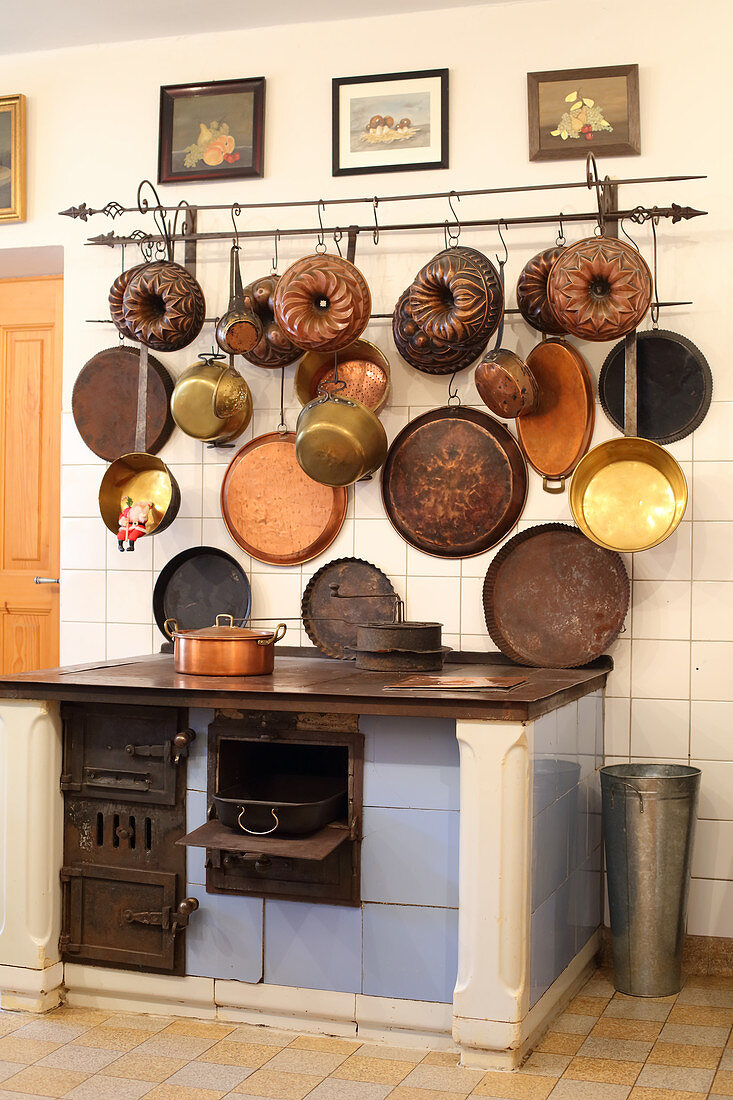 Alter Holzofen, darüber Vintage Pfannen und Backformen in der Küche