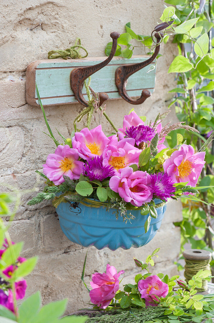 Early summer bouquet of roses, knapweeds, and grasses hung in an enameled baking pan