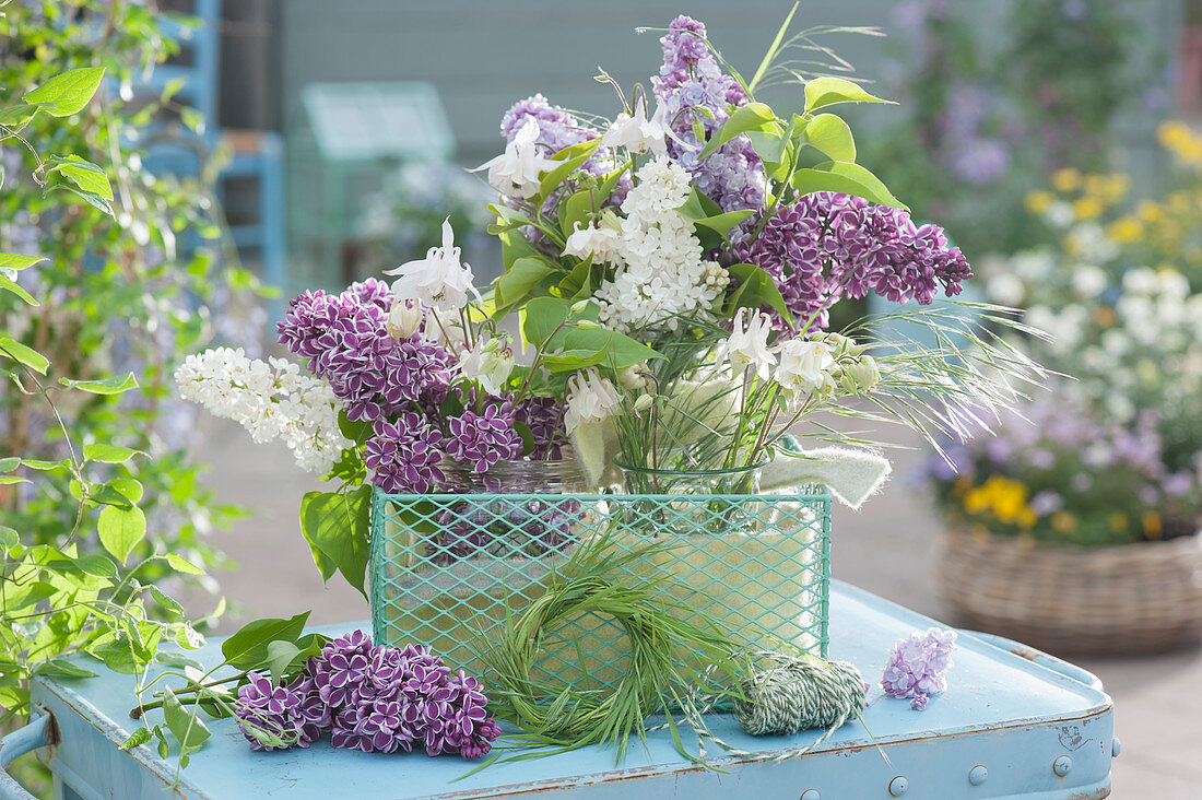 Small bouquets of lilac flowers, columbine, and grass in a wire basket