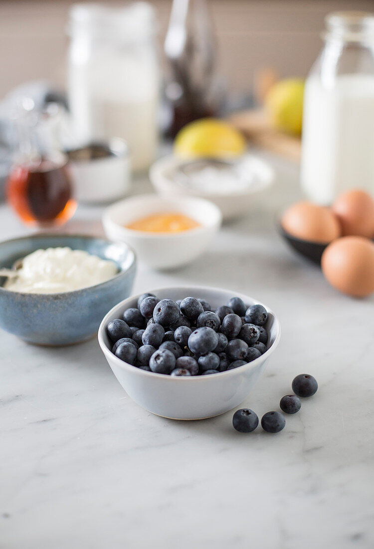 A bowl of blueberries, with pancake batter in the background