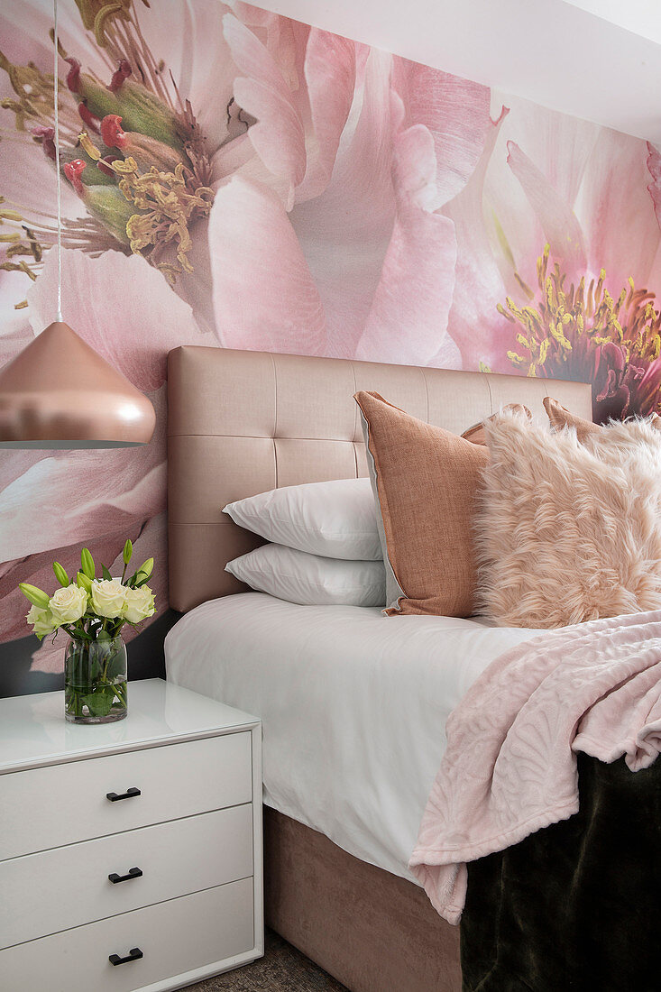 Double bed with button-tufted headboard, bedside cabinet below pendant lamp and wallpaper with huge floral motif in bedroom