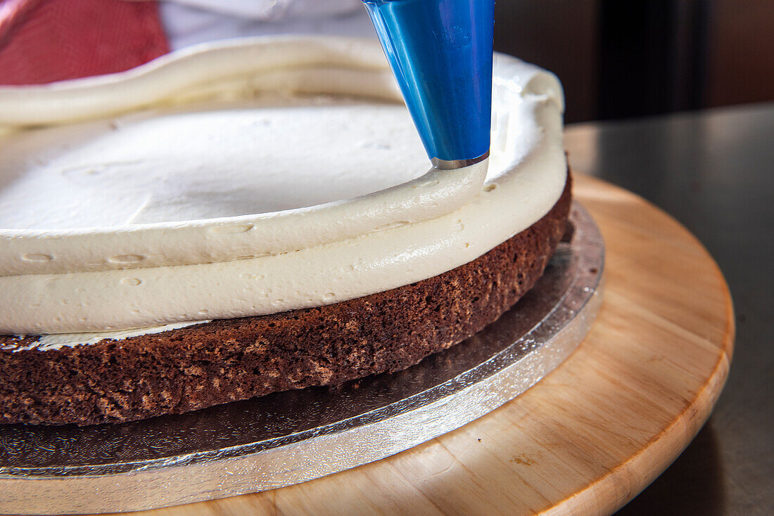 Piping vanilla buttercream onto the chocolate base of a wedding cake