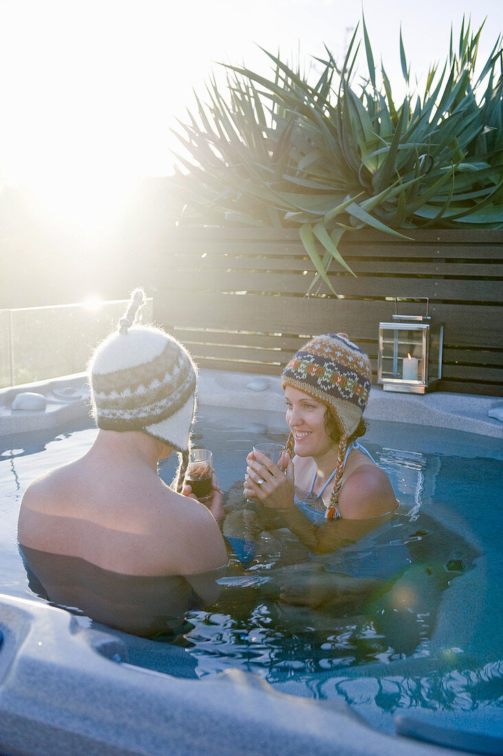 Man and woman wearing woolly hats in pool in sunshine