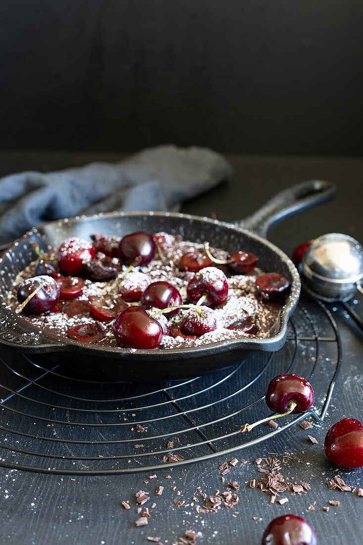 Schokoladen-Clafoutis mit Kirschen und Puderzucker in Pfanne