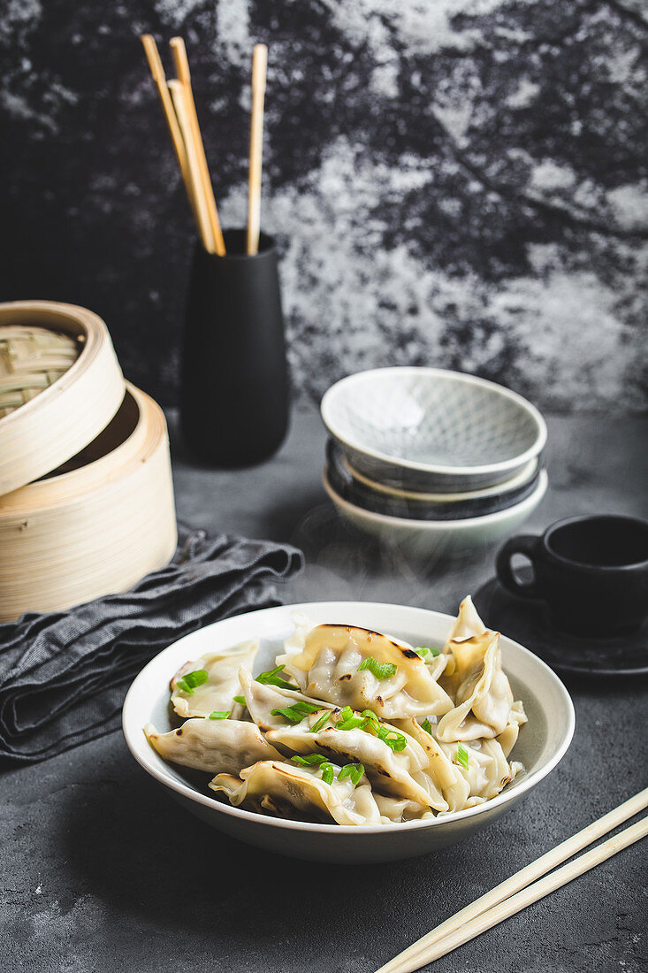 Asian dumplings in bowl, chopsticks, bamboo steamer, plates