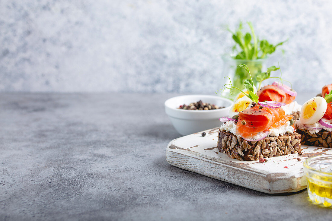 Close-up of sandwich with dark rye bread, cream cheese, salmon, onion, boiled egg on white wooden cutting board