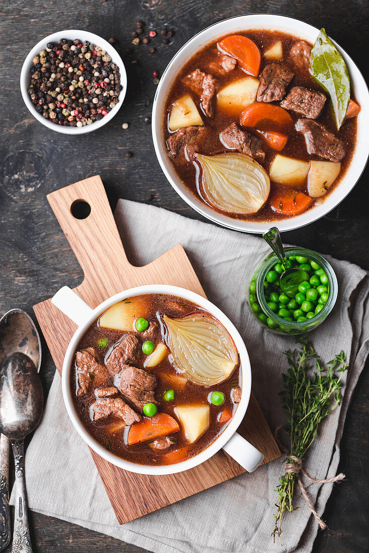 Meat stew with beef, potato, carrot, pepper, spices, green peas. Slow cooked meat stew, bowl, wooden background
