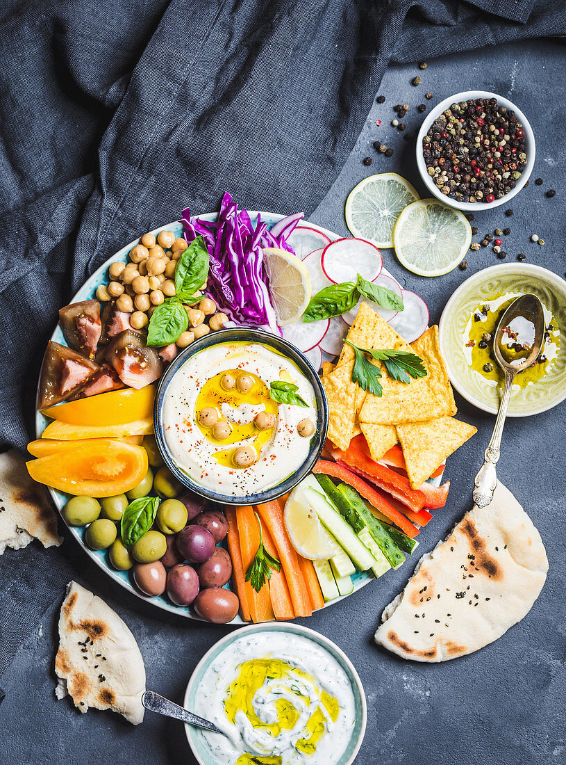 Meze platter with hummus, yoghurt dip, assorted snacks: Hummus in bowl, vegetables sticks, chickpeas, olives, pita, chips