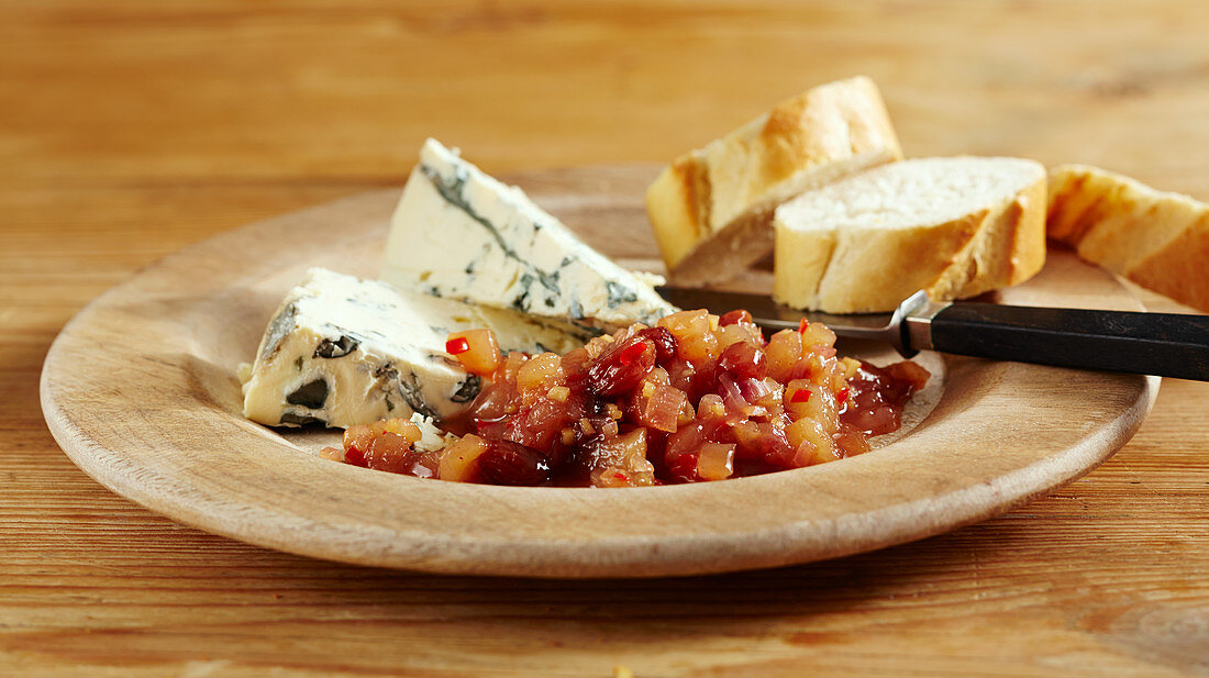 Sweet pear chutney with chili served with blue cheese and sliced baguette on a wooden dish