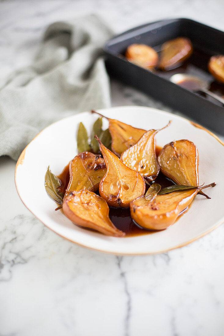 Baked pears with bay leaves on a plate and in a baking dish