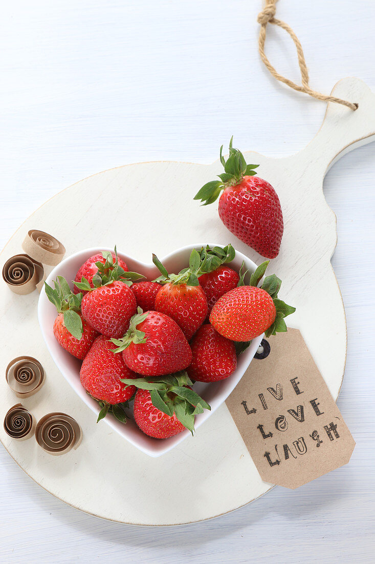 Frische Erdbeeren in Herzschale mit Botschaft auf weissem Brett