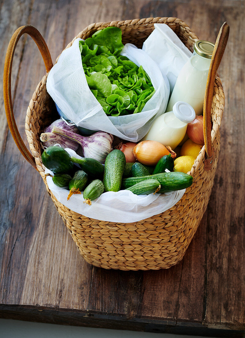 A basket bag with lettuce, vegetables, lemons, milk, cream and oatmeal