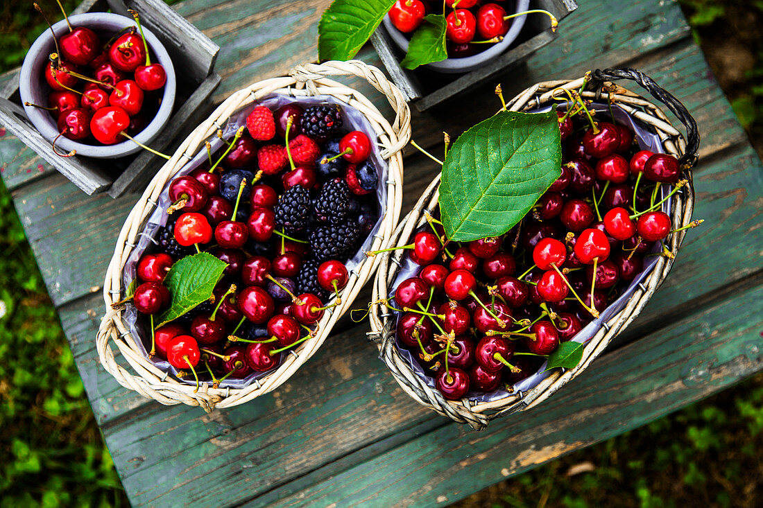 Fresh organic cherries, blueberries and blackberries in baskets on a wooden table