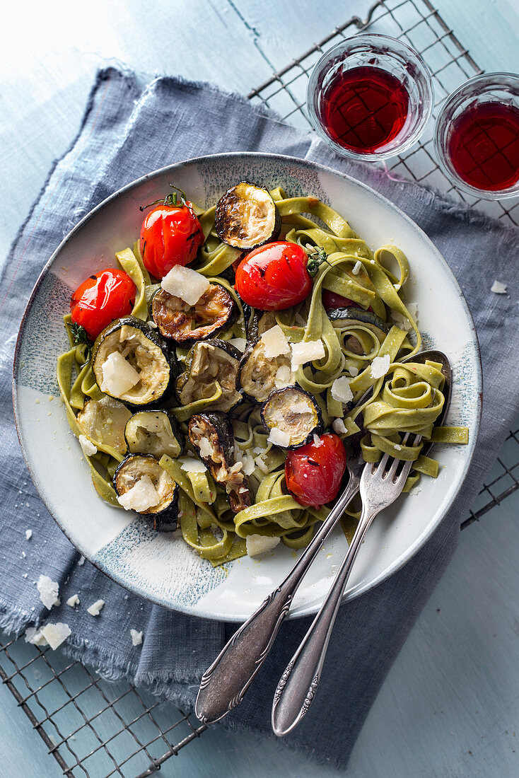 Grüne Bandnudeln mit gegrillten Zucchini, Cocktailtomaten und Parmesan auf blauem Holzuntergrund