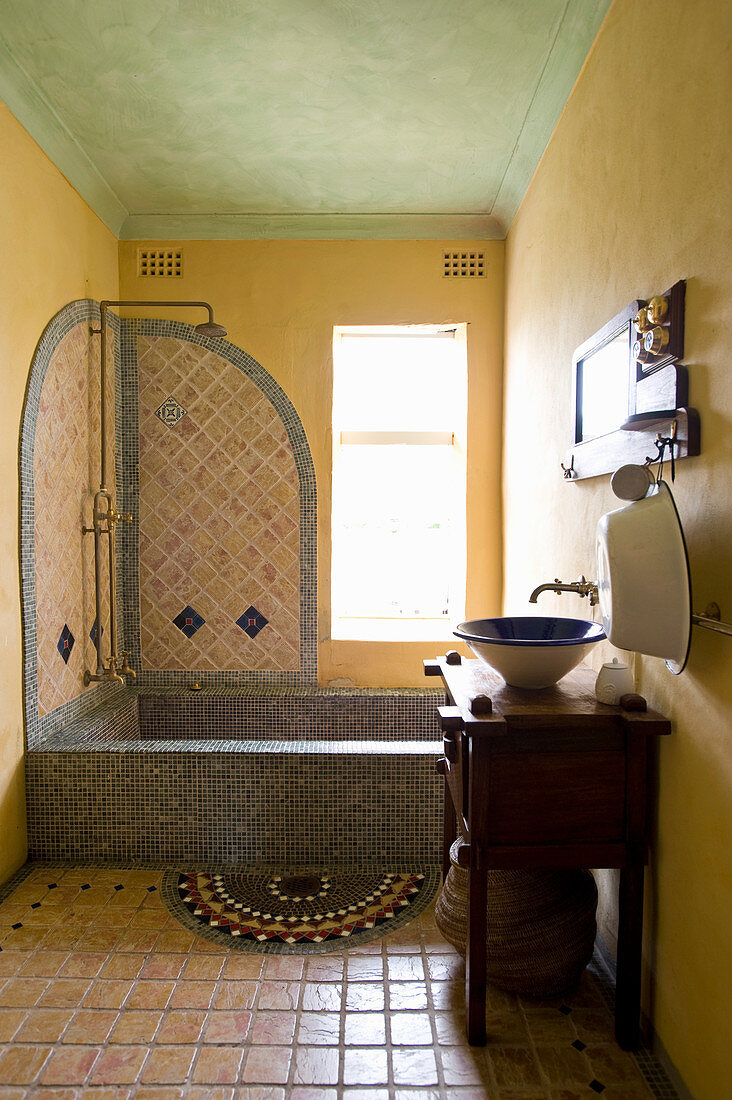 Mosaic-tiled bathtub in Oriental bathroom with yellow walls
