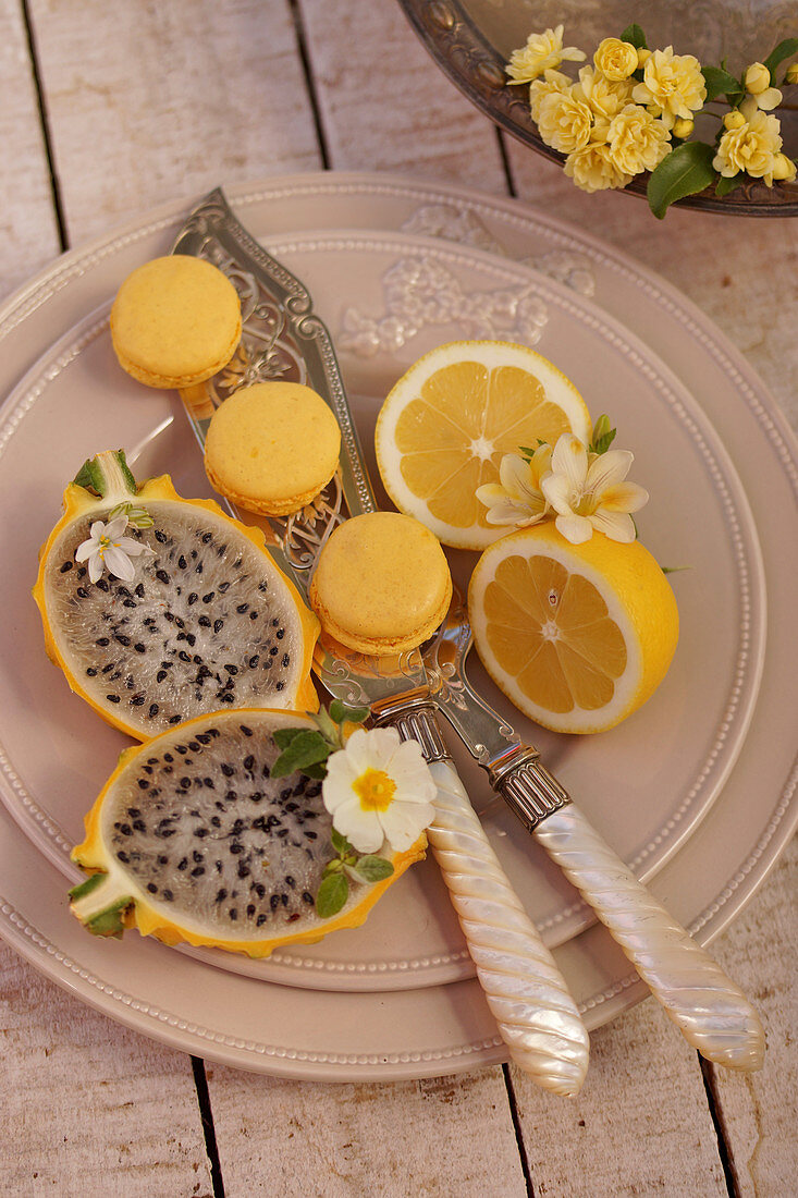 Zitronenmacarons, gelbe Drachenfrucht und halbierte Zitrone auf Teller