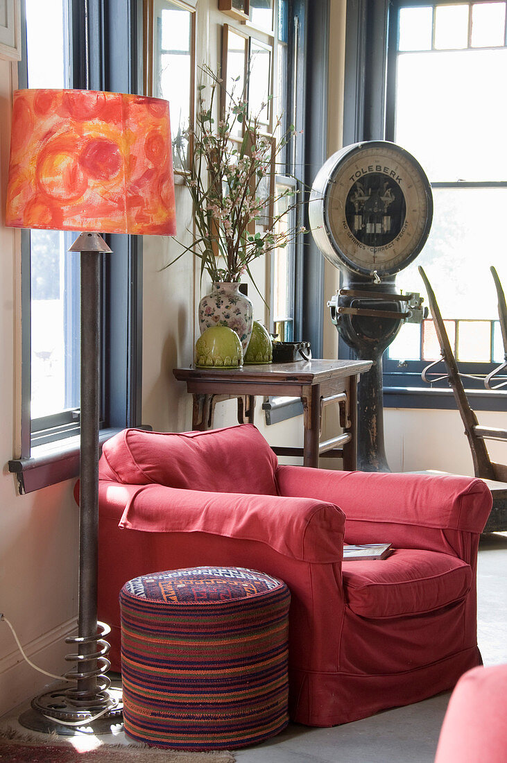 Red armchair, pouffe and standard lamp in front of console table and vintage scales