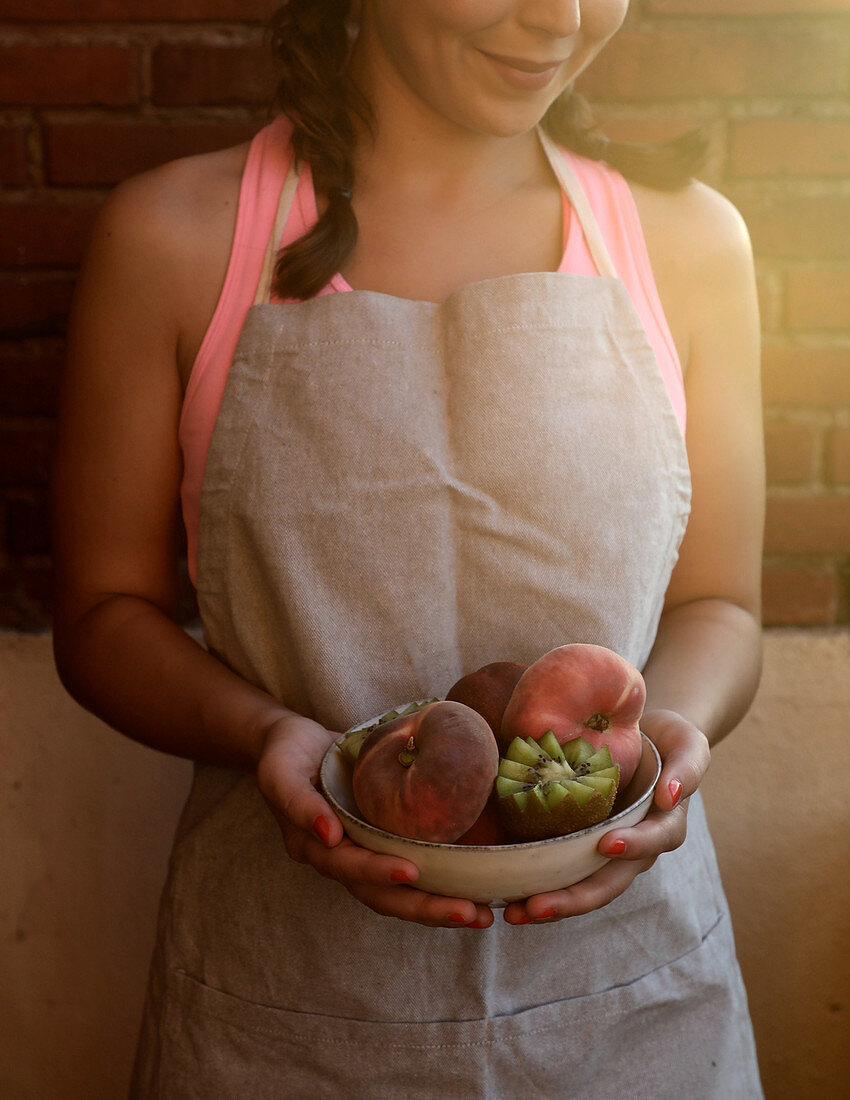 Junge Frau mit frischen Pfirsichen und Kiwis in einer Keramikschale