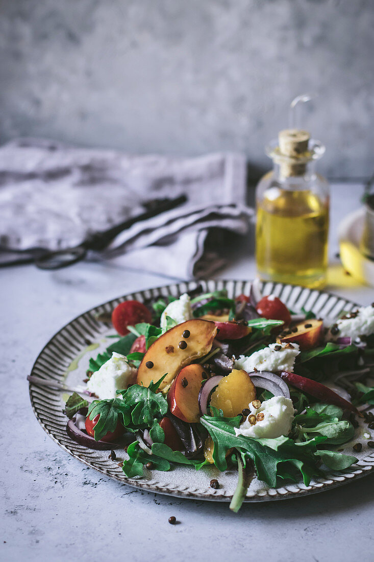 From above plate with gourmet salad made of peaches, red onion, oil and black pepper on white background