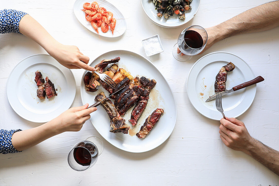 Hands cutting meat steak and enjoying red wine while eating tasty meal