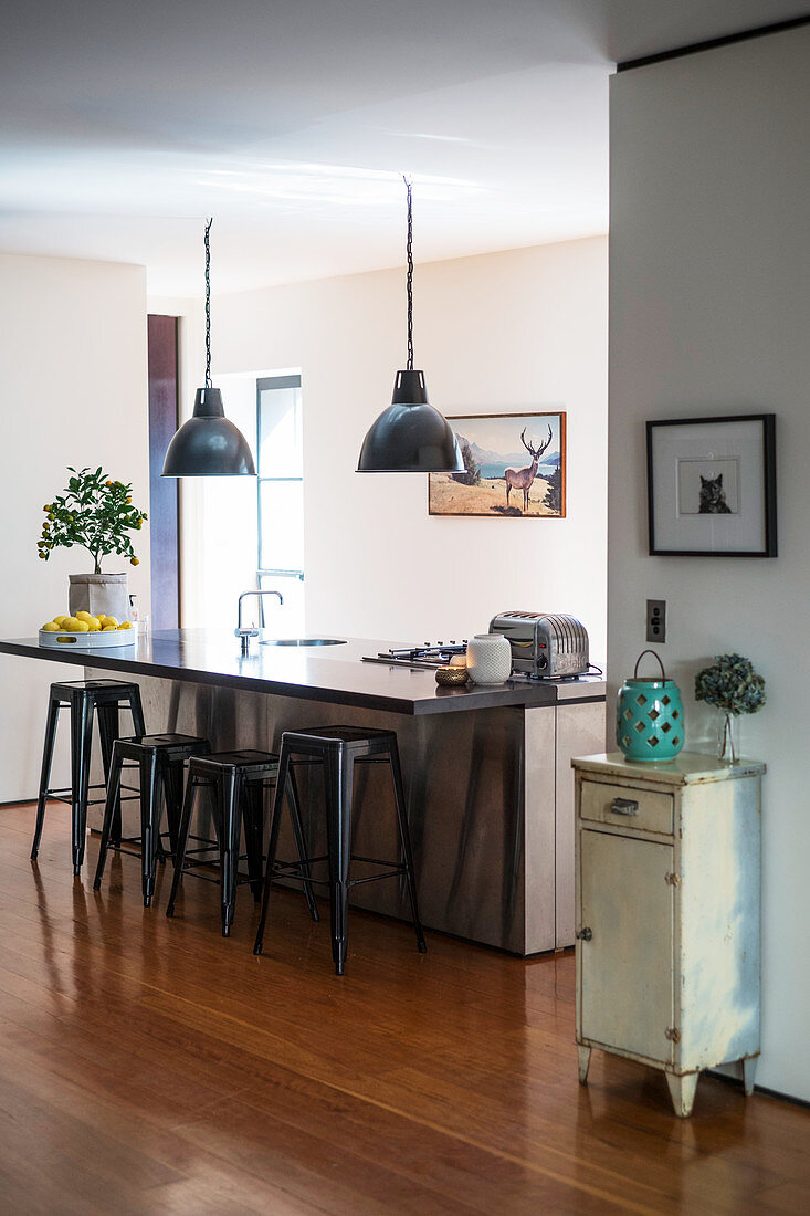 Island counter with bar stools below industrial lamps in open-plan kitchen