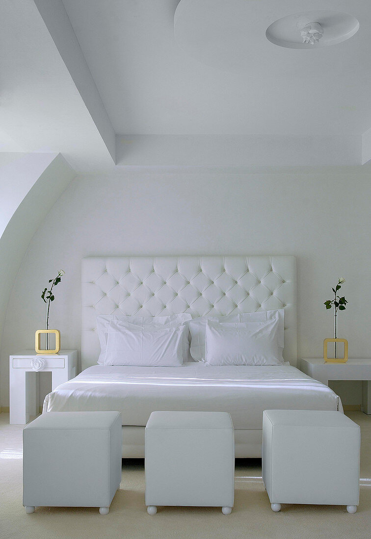 Double bed with white headboard and white cubic pouffes in bedroom