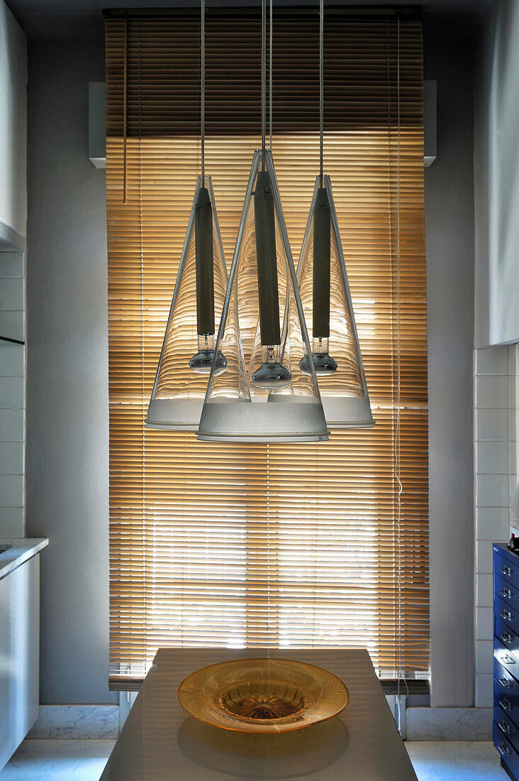 Designer lamps above dining table in open-plan kitchen with louvre blind in background