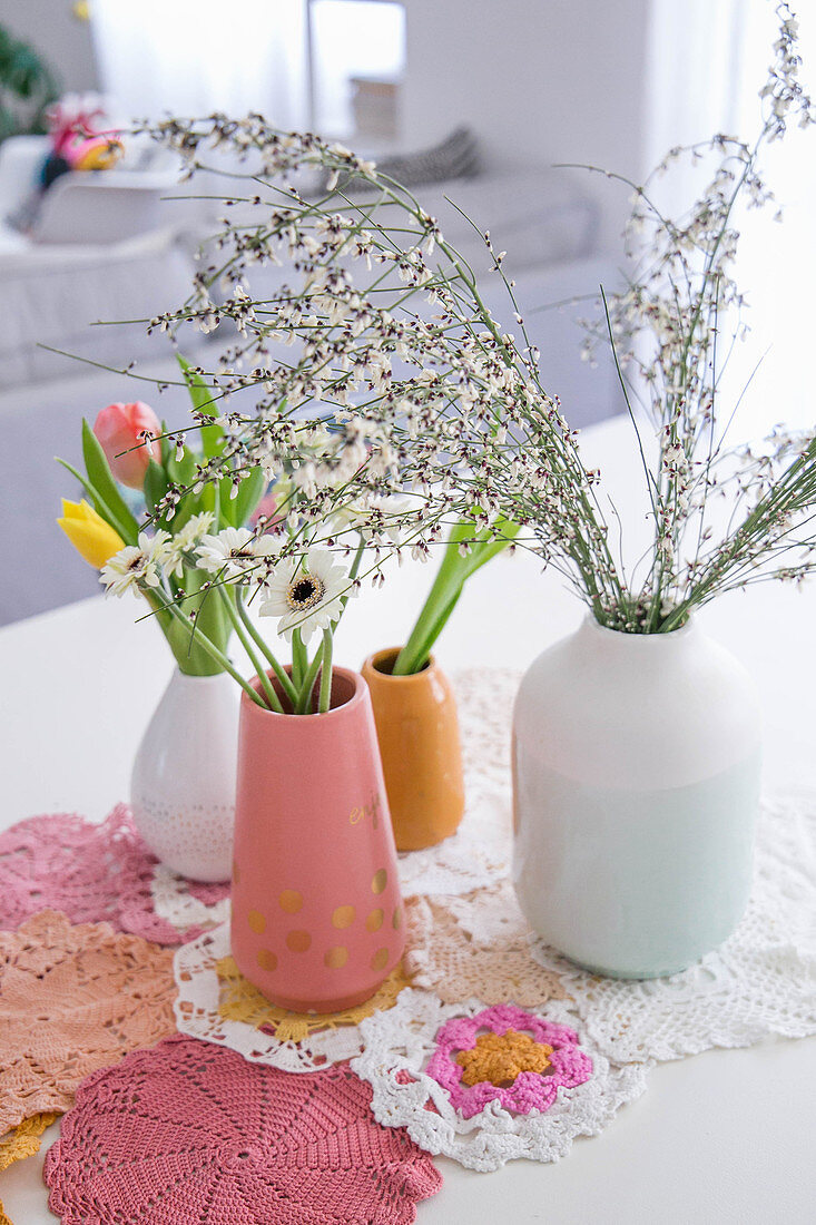 Vases of spring flowers and crocheted doilies on dining table