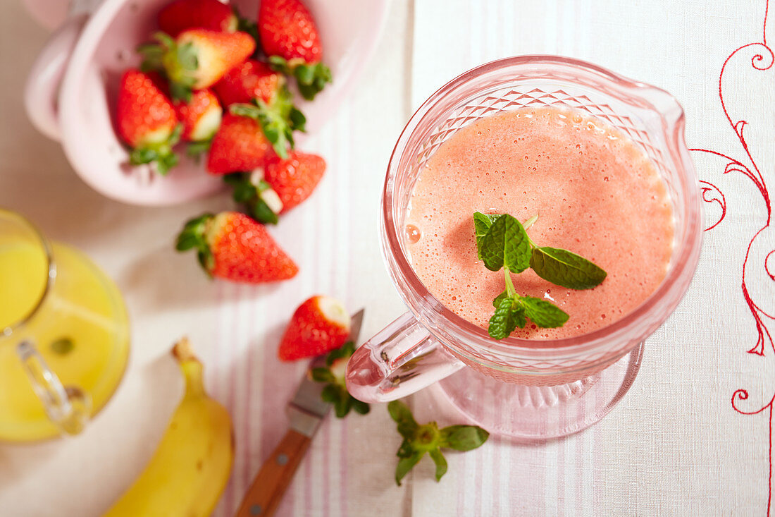 Erdbeer-Smoothie mit Banane, Orangensaft, Minze und Honig in Glaskrug