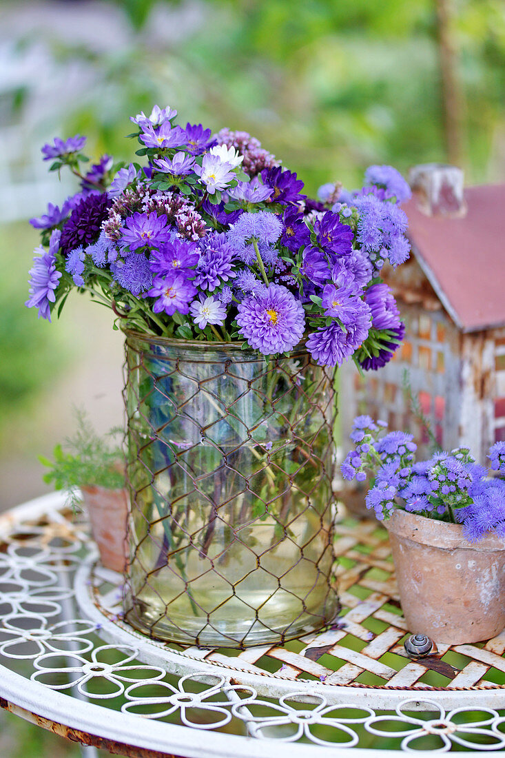 Bouquet of asters, floss flowers and verbena in glass vase on garden table