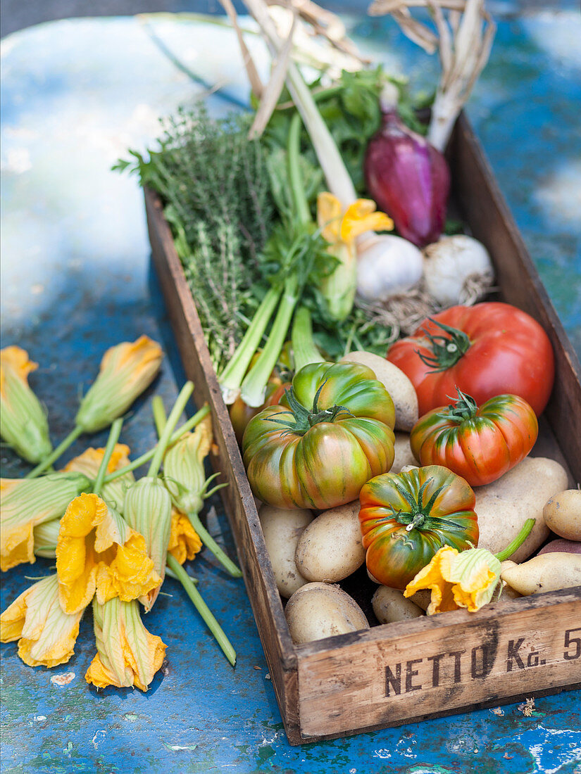 Gemüsekiste mit Tomaten, Kartoffeln und Zucchiniblüten