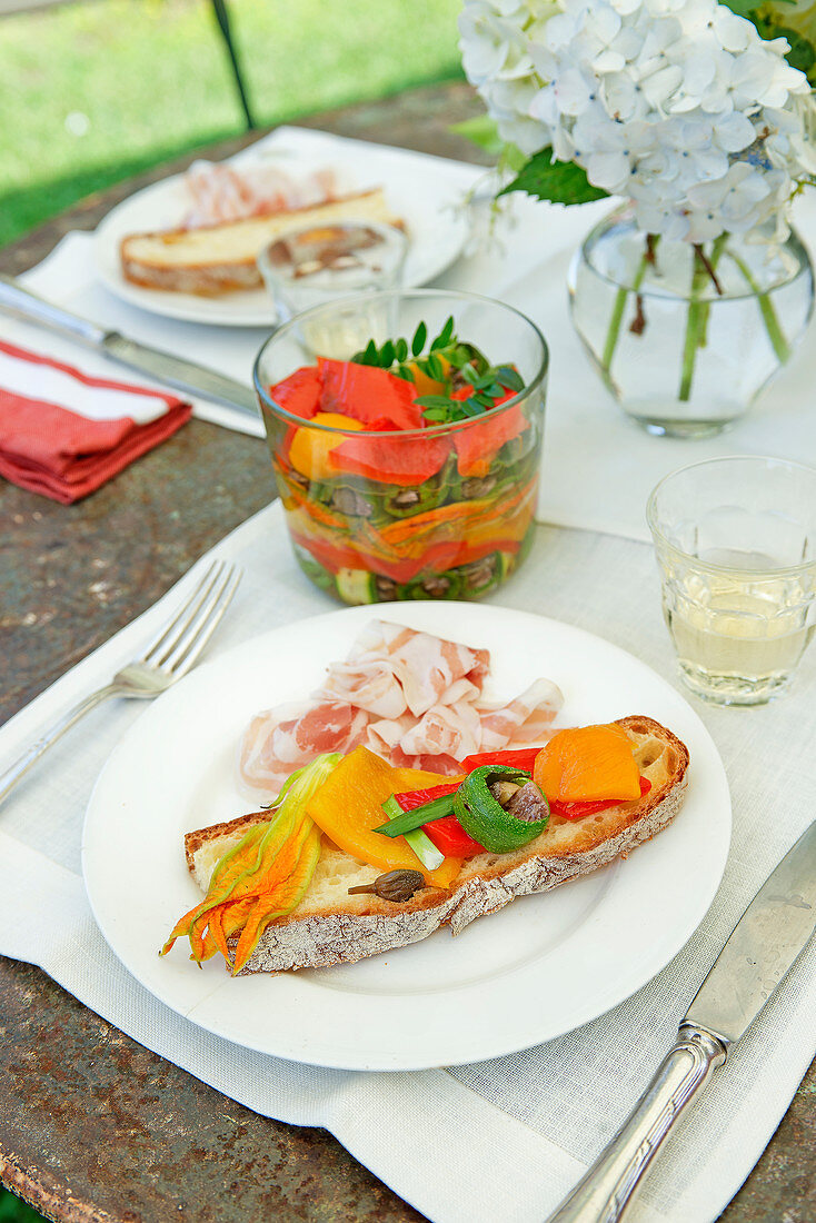 Antipasti aus Paprika, Zucchini und Zucchiniblüten auf Brot
