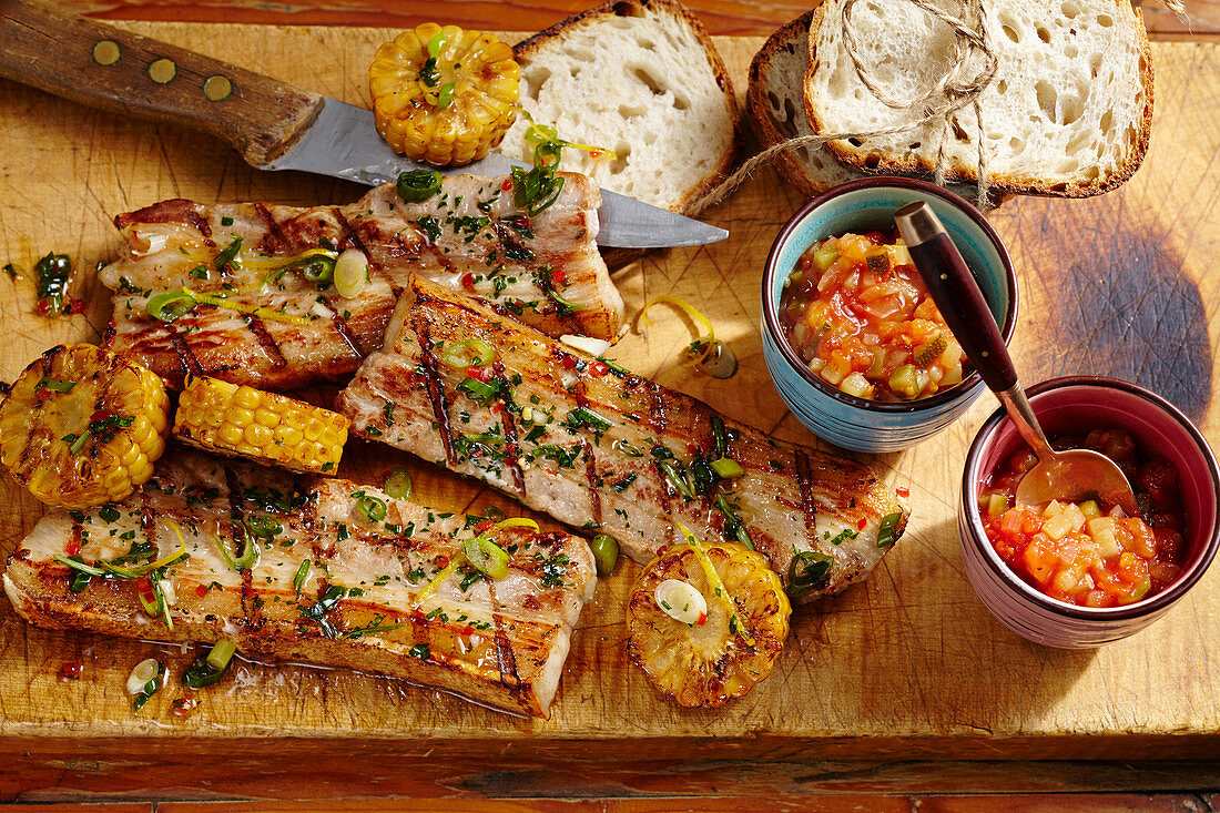 Grilled pork belly slices with a tomato and courgette chutney, corn cobs and white bread